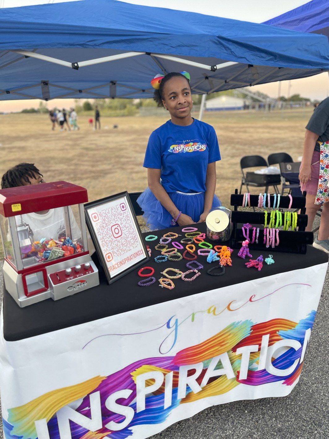 Grace standing proudly behind her colorful bracelet booth